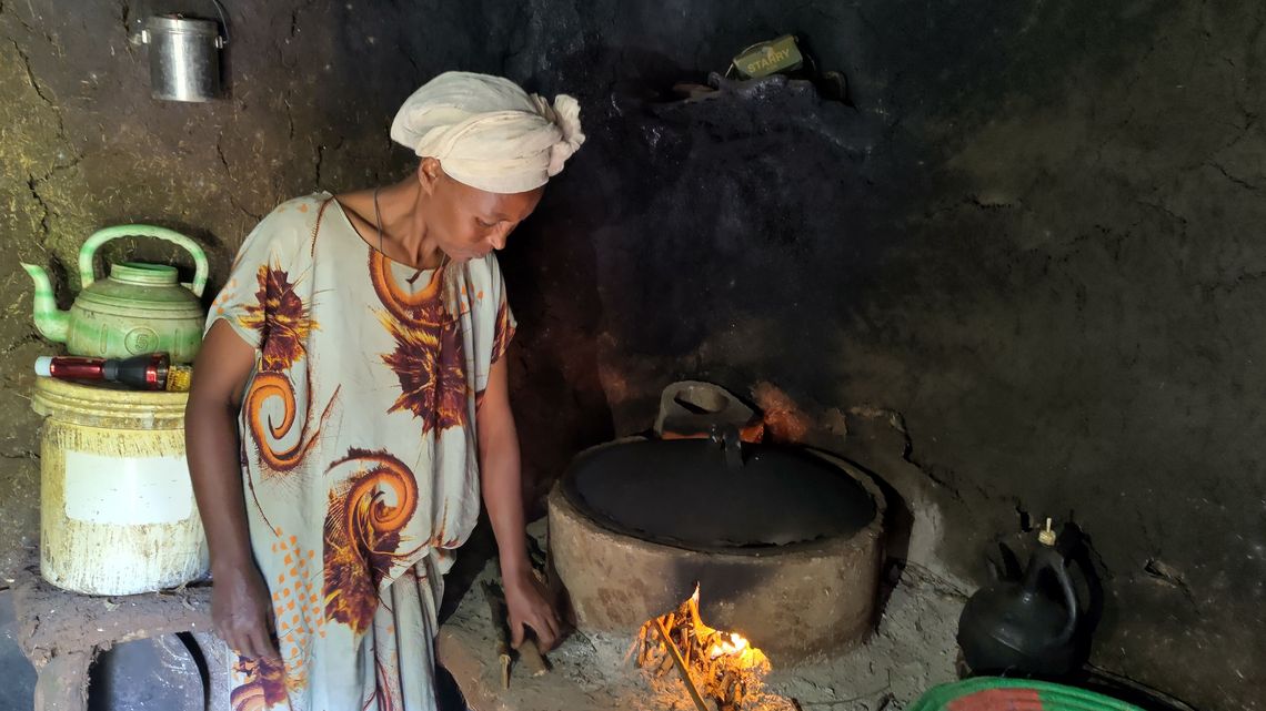 Eine Frau im inneren eines Hauses vor einem angeheizten Ofen.
