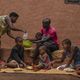 Zwei Erwachsene und vier Kinder sitzen vor ihrem Haus und nehmen eine Mahlzeit ein. 