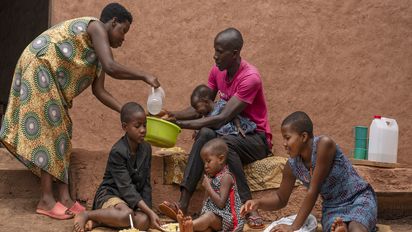 Zwei Erwachsene und vier Kinder sitzen vor ihrem Haus und nehmen eine Mahlzeit ein. 