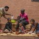 Zwei Erwachsene und vier Kinder sitzen vor ihrem Haus und nehmen eine Mahlzeit ein. 