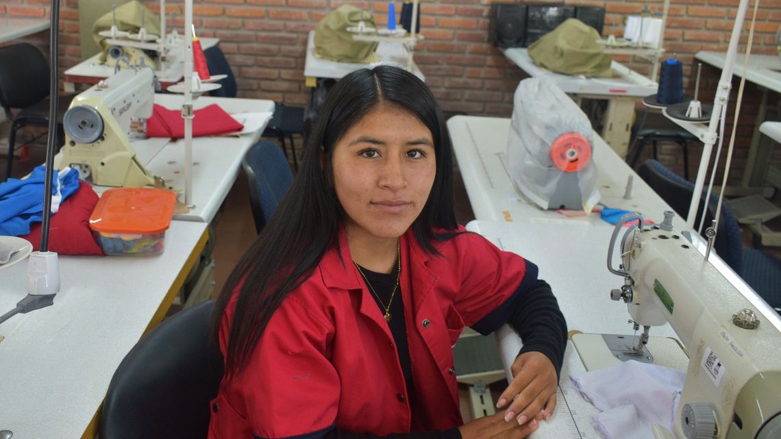 Eine Frau vor einer Nähmaschine, lächelt in die Kamera.