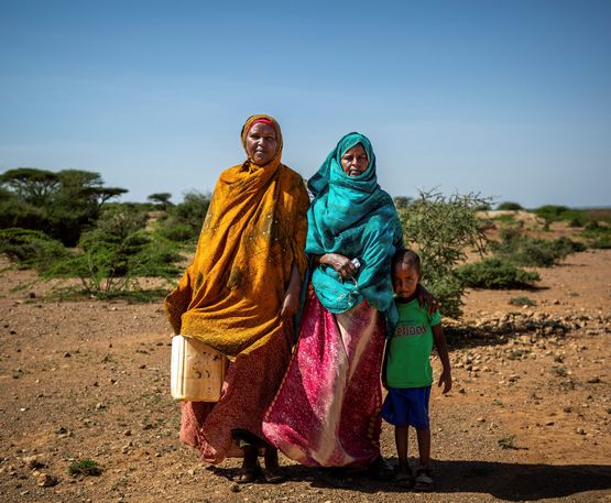 Zwei Frauen mit Kleinkind in karger Landschaft, eine der Frauen trägt einen Wasserkanister