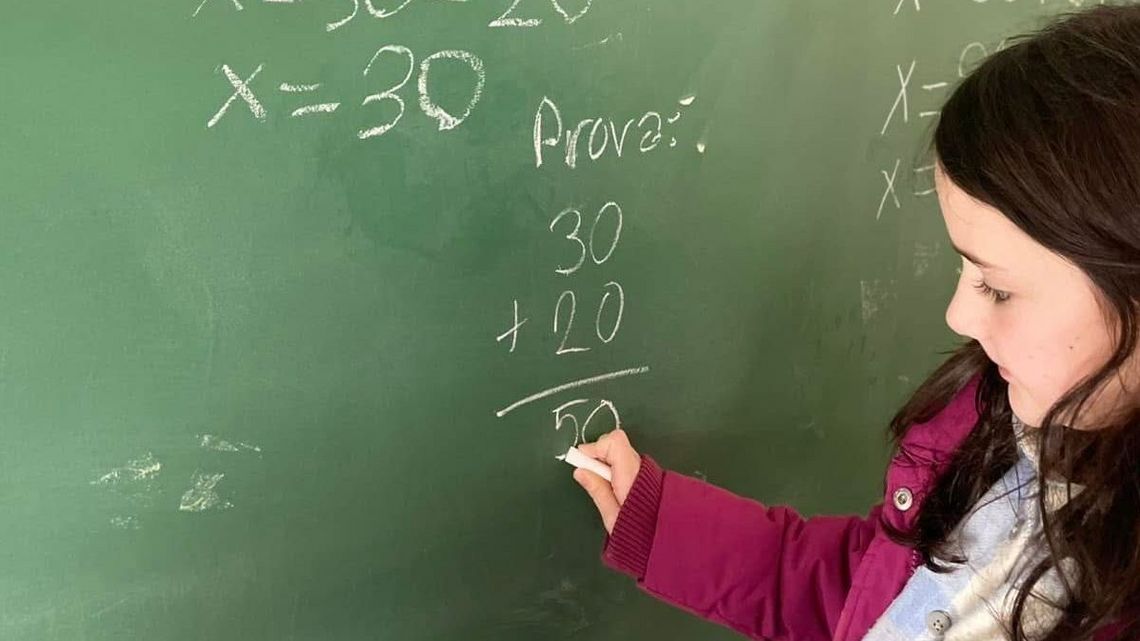 Eine junge Schülerin schreibt mit Kreide Zahlen auf eine grüne Tafel. 