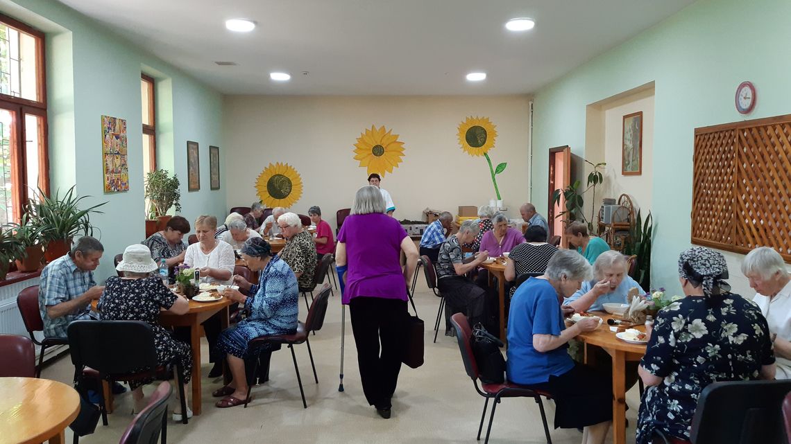 In einem großen, freundlichem Raum sitzen ältere Menschen an Tischen und essen.