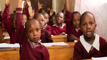 Kinder in roten Schuluniformen sitzen hinter Schulbänken.