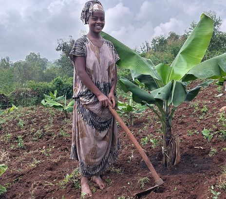 Frau bei der Feldarbeit neben einer Bananenpflanze. 