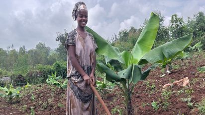 Frau bei der Feldarbeit neben einer Bananenpflanze. 